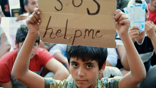 Ni&ntilde;o inmigrante sostiene un cartel en el que se lee &#039;SOS ay&uacute;dame&#039; mientras se sienta con otros migrantes en Keleti. (V&iacute;a: AFP)