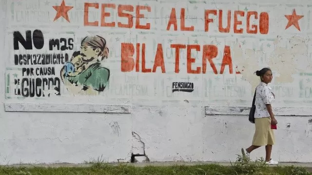 Una mujer camina por un mural que reza "Cese al fuego bilateral" en una calle de El Palo. (Vía: AFP)