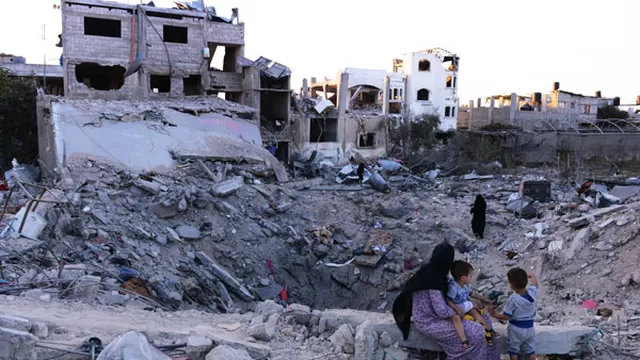 Una madre se sienta junto a sus dos hijos en un cr&aacute;ter donde sol&iacute;a estar su casa. Ahora, totalmente destruida por los ataques israel&iacute;es. (Foto: AFP)