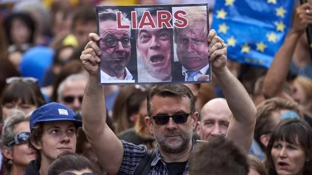 Un hombre sostiene un cartel con las caras de Michael Gove, Nigel Farage y Boris Johnson. (Vía: AFP)